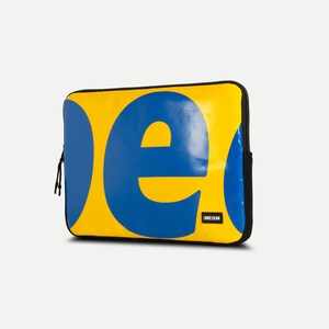 May include: Yellow laptop sleeve with a blue "e" and a blue circle. The sleeve has a black zipper and the text "LINEEUNO" in black.