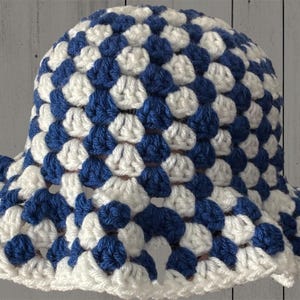 May include: A handmade crochet hat in a checkerboard pattern of white and navy blue. The hat has a wide brim and a rounded crown. The crochet stitches are visible, giving the hat a textured appearance. The hat is likely for sun protection.