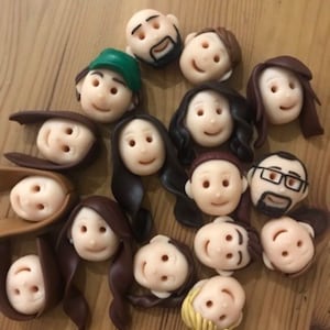 May include: A collection of 15 handmade clay figurines of people with different hairstyles and facial expressions. The figurines are all in various shades of brown, white, and black.