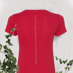 May include: Red short-sleeved t-shirt with a vertical quote in gold lettering on the back: "In the end, some of your greatest pain becomes your greatest strength."