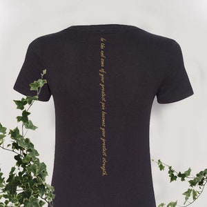 May include: Black t-shirt with a gold inscription that reads "In the end, some of your greatest pain becomes your greatest strength."