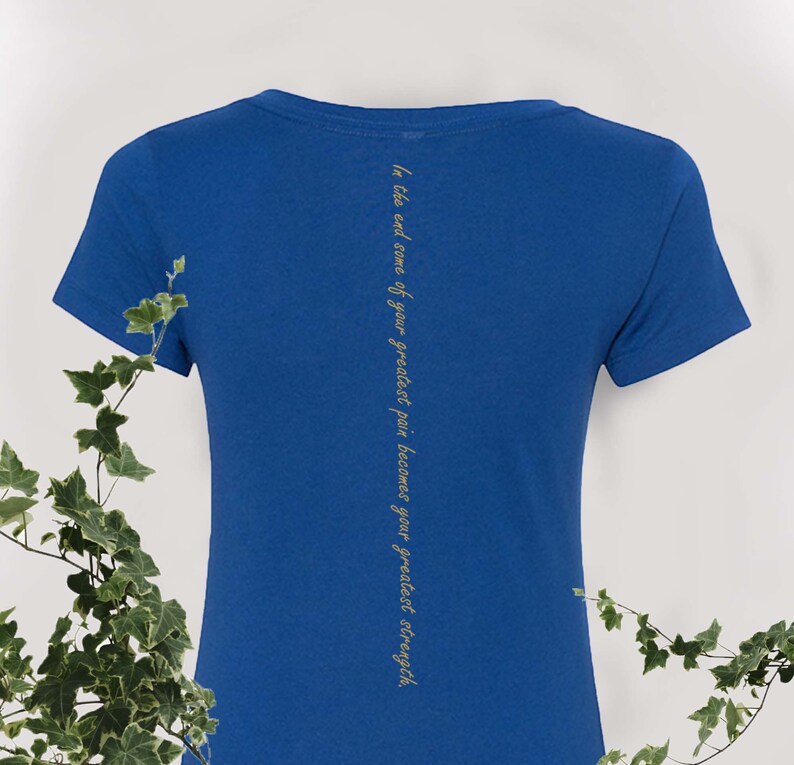 May include: A royal blue t-shirt with a gold inscription on the back that reads "In the end some of your greatest pain becomes your greatest strength."