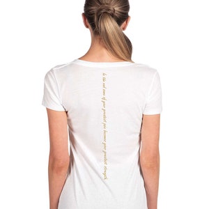 May include: White v-neck t-shirt with the text "In the end, we are our greatest pain because our greatest strength." printed on the back.