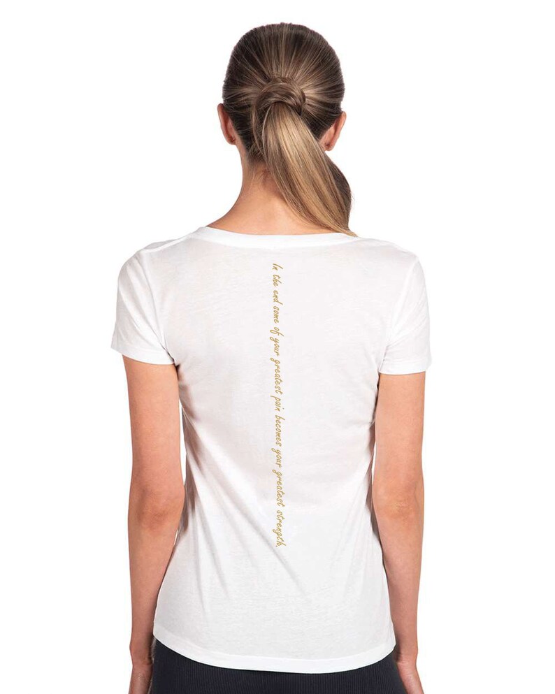 May include: White v-neck t-shirt with the text "In the end, we are our greatest pain because our greatest strength." printed on the back.