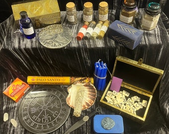May include: A collection of witchy items including a wooden box with a pentagram design, a set of runes, a palo santo stick, a seashell, a knife, a small tin with a rune symbol, and a set of blue candles.