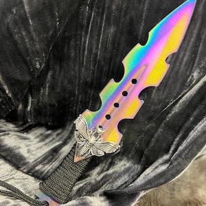 May include: A iridescent rainbow colored dagger with a black paracord handle and a silver moth design on the blade.