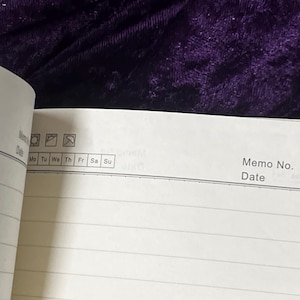 May include: Open notebook with lined pages, featuring a section for memo details and a date. The top section includes icons and the days of the week, from Monday to Sunday. The background is a dark purple velvet.