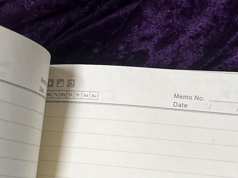 May include: Open notebook with lined pages, featuring a section for memo details and a date. The top section includes icons and the days of the week, from Monday to Sunday. The background is a dark purple velvet.