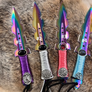 May include: Four iridescent daggers with different colored handles and decorative accents. The handles are purple, white, pink, and blue. Each dagger has a different symbol on the handle. The daggers are numbered 1 through 4.