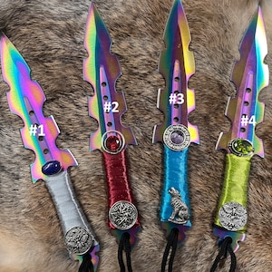 May include: Four iridescent daggers with decorative handles. Each handle features a different colored gemstone, a metal emblem, and a black cord. The daggers are numbered 1 through 4.