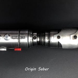 Puede incluir: Un sable de luz plateado con un mango negro y un bot&oacute;n rojo. El sable de luz tiene una carcasa de metal plateado con un agarre negro y un bot&oacute;n rojo en el lateral. El sable de luz es un juguete popular para los fan&aacute;ticos de la franquicia Star Wars.