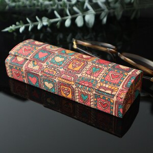 May include: A rectangular glasses case with a colorful pattern of hearts and squares. The case is made of cork and has a brown background with red, orange, yellow, blue, and green accents.