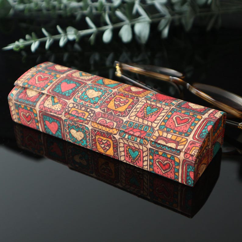 May include: A rectangular glasses case with a colorful pattern of hearts and squares. The case is made of cork and has a brown background with red, orange, yellow, blue, and green accents.