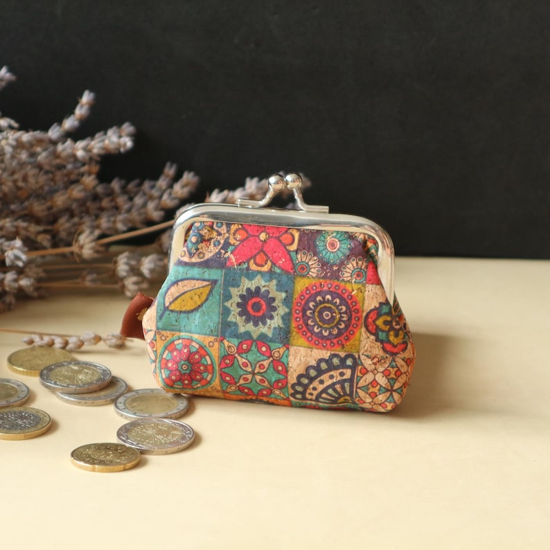 May include: A small, colorful coin purse with a floral pattern. The purse is made of cork and has a silver metal frame.