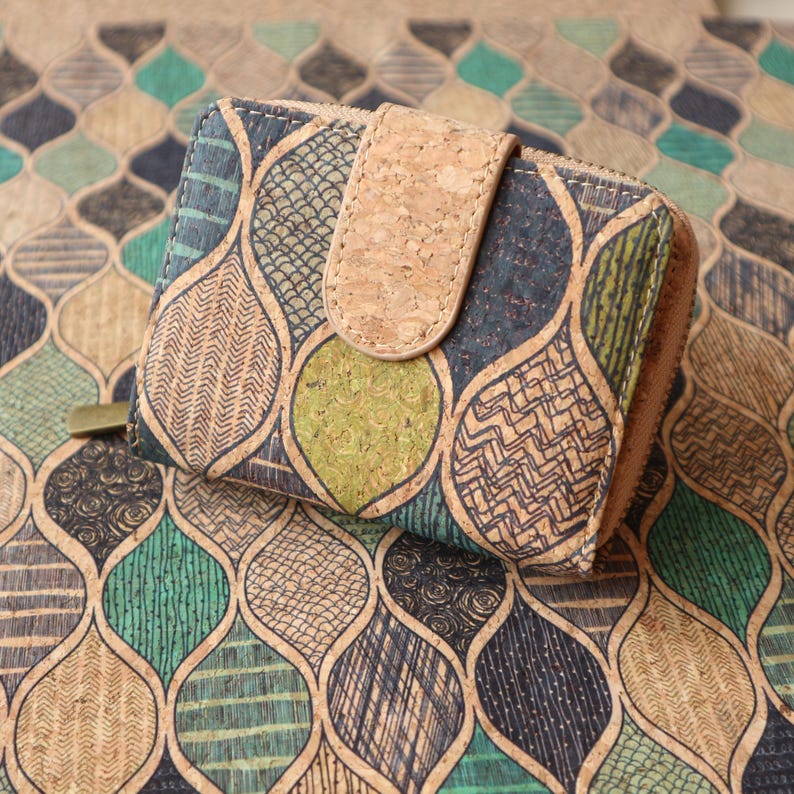 Op de afbeelding: Een portemonnee van kurk met een geometrisch patroon van groene, bruine en zwarte bladeren. De portemonnee heeft een klep sluiting met een bruine kurkband.