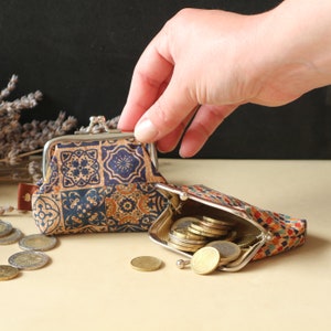 May include: Two small coin purses with a blue and brown patterned design. One purse is open and filled with coins. The purses are made of cork and have a metal frame.