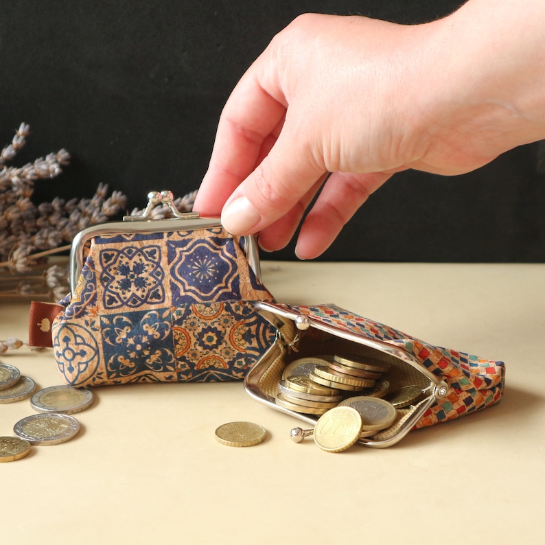 May include: Two small coin purses with a blue and brown patterned design. One purse is open and filled with coins. The purses are made of cork and have a metal frame.