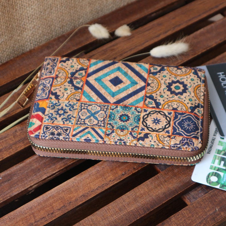 May include: A brown zippered wallet with a colourful patterned design. The pattern features a variety of geometric shapes and designs in shades of blue, green, orange, and yellow. The wallet is made of cork and has a zipper closure.
