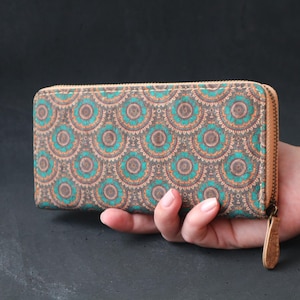Puede incluir: Una cartera de corcho marrón con cierre de cremallera y un patrón geométrico azul verdoso y naranja.