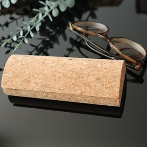 May include: A light brown cork eyeglasses case with a rounded shape. The case is made of natural cork and has a smooth, textured surface.