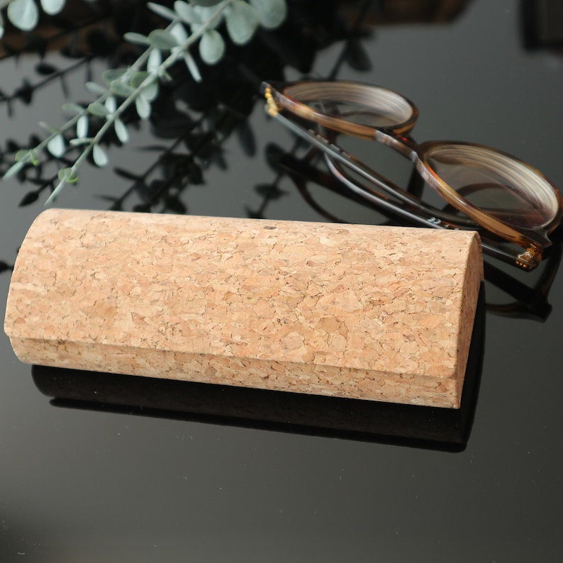 May include: A light brown cork eyeglasses case with a rounded shape. The case is made of natural cork and has a smooth, textured surface.