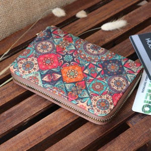 May include: A colourful zippered wallet with a patterned design featuring geometric shapes and floral motifs in shades of red, orange, blue, green, and brown.
