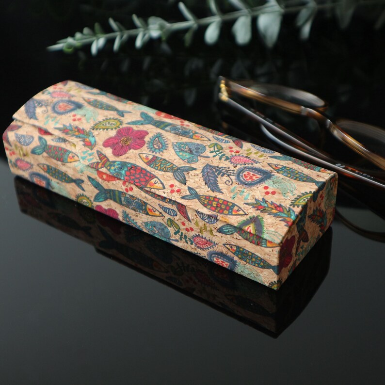 May include: A rectangular cork eyeglasses case with a colorful pattern of fish, flowers, and paisley designs. The case is closed and sitting on a black surface.
