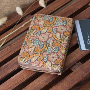 May include: A zippered wallet with a colourful paisley pattern. The wallet is made of cork and has a brown zipper.