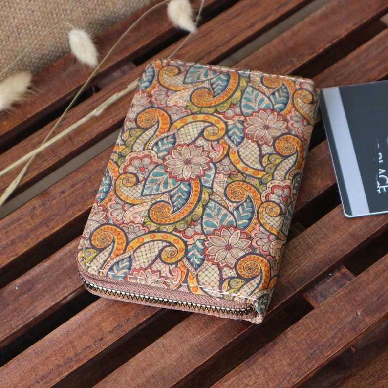 May include: A zippered wallet with a colourful paisley pattern. The wallet is made of cork and has a brown zipper.
