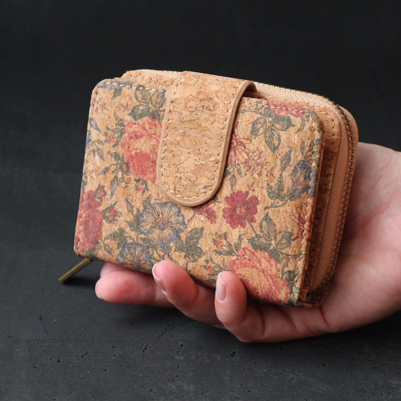 Op de afbeelding: Een kleine, bloemenprint portemonnee gemaakt van kurk met een ritssluiting. De portemonnee heeft een bruine kurk flap met een drukknopsluiting.