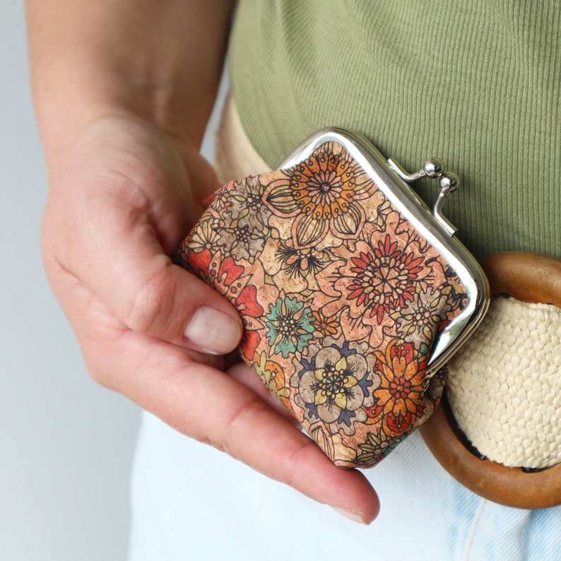 May include: A small, floral patterned coin purse with a silver metal frame and a snap closure. The purse is held in a person's hand.