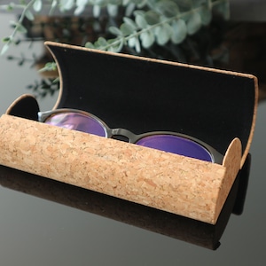 May include: A cork eyeglasses case with a black velvet interior. The case is open and a pair of glasses with purple lenses are inside.