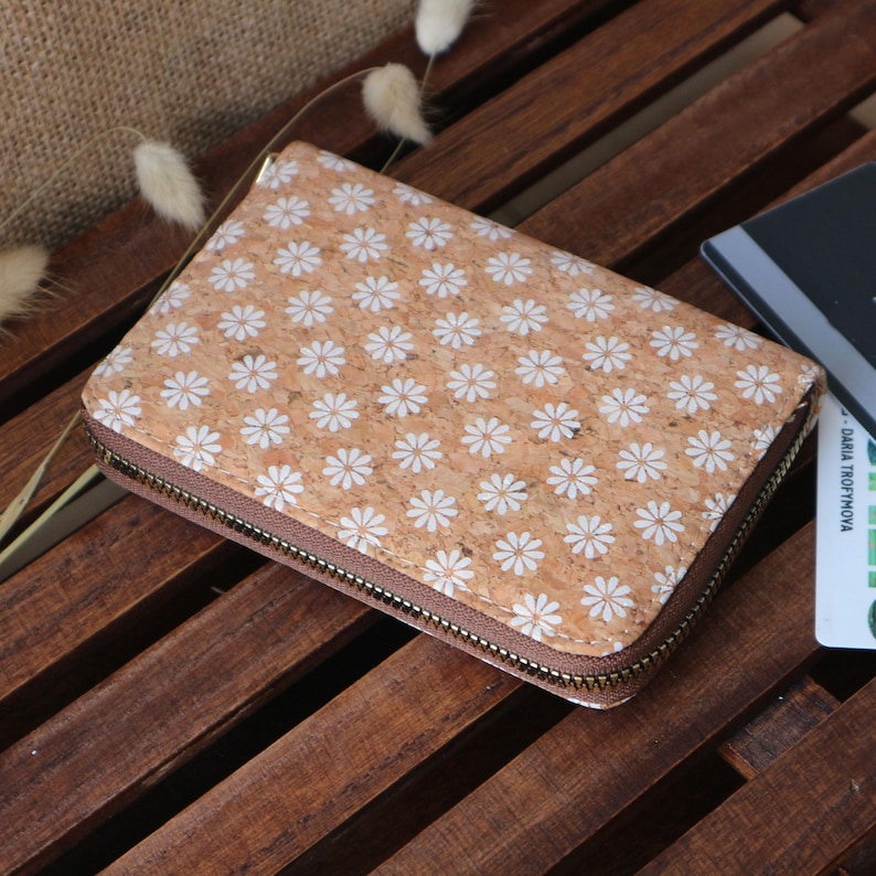 May include: A brown cork wallet with a white daisy pattern and a zipper closure.