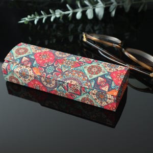 May include: A rectangular glasses case with a colorful patterned design featuring geometric shapes and floral motifs in shades of red, blue, green, and beige.