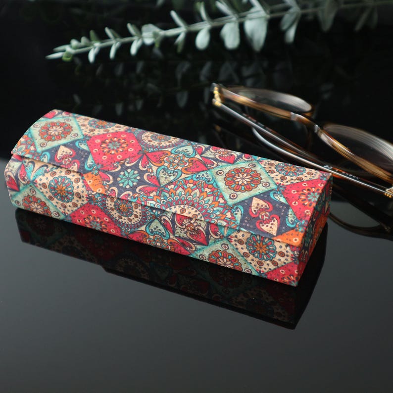 May include: A rectangular glasses case with a colorful patterned design featuring geometric shapes and floral motifs in shades of red, blue, green, and beige.