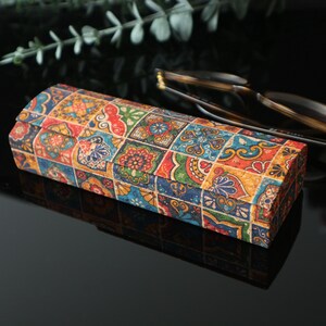 May include: A colorful rectangular glasses case with a patterned design of colorful tiles. The case is made of hard plastic or wood and has a hinged lid.