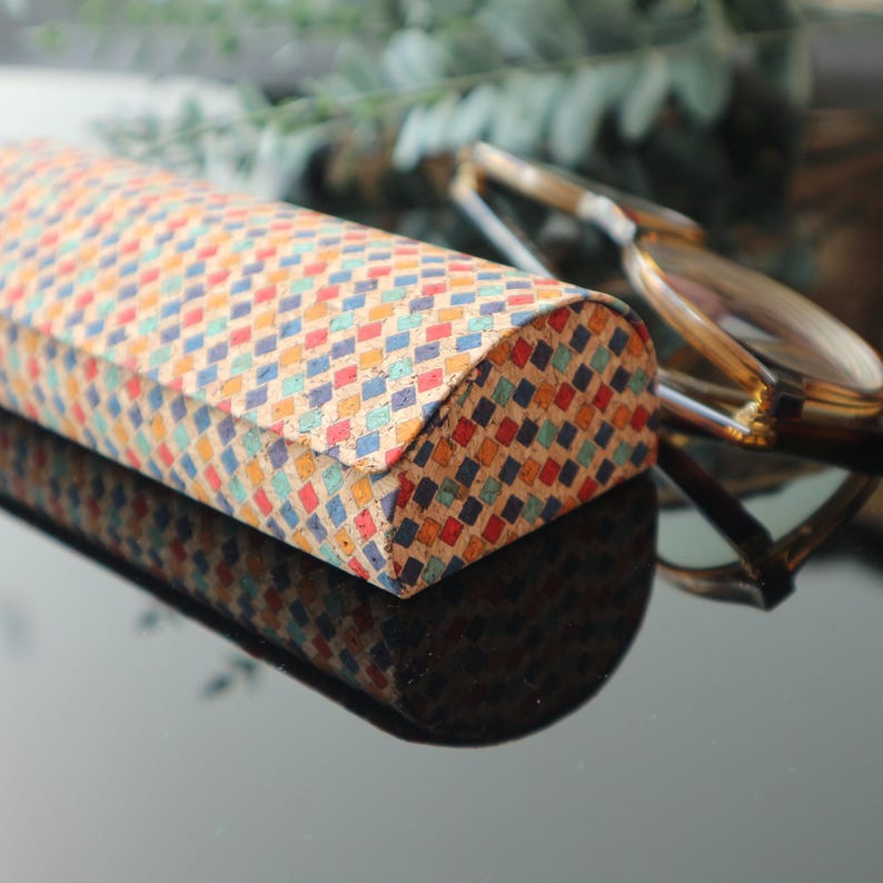 May include: A colorful, patterned, cork eyeglass case with a curved top. The case is made of cork and has a geometric pattern in shades of blue, red, orange, and yellow.