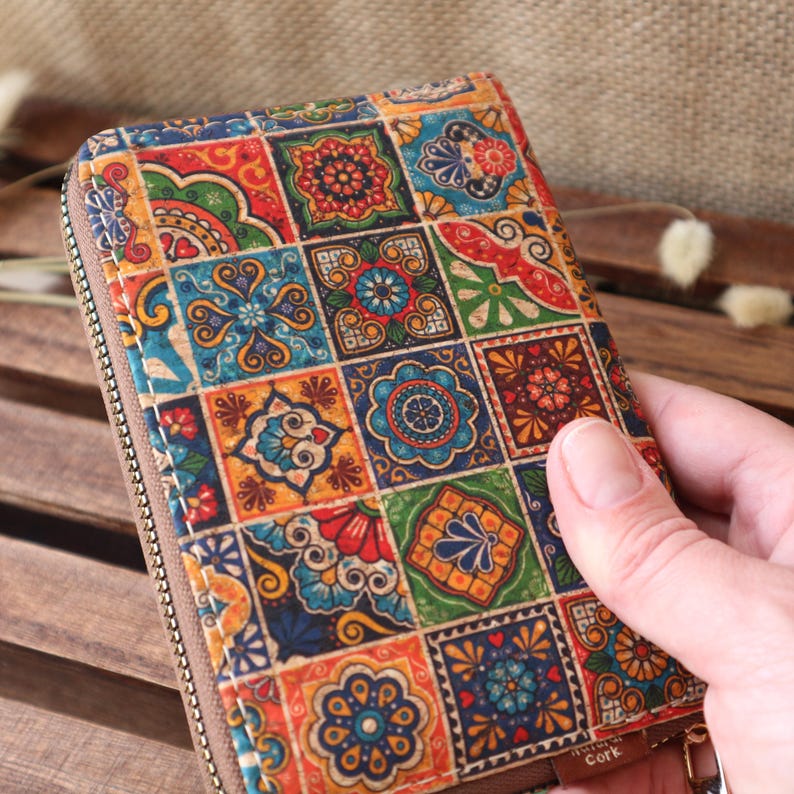 May include: A colourful zippered wallet with a patchwork design of colourful squares with floral patterns. The wallet is made of cork and has the word "Cork" printed on the bottom.