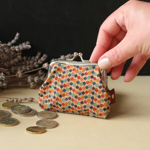May include: A small, colorful coin purse with a geometric pattern. The purse is made of cork and has a silver metal frame with a snap closure.