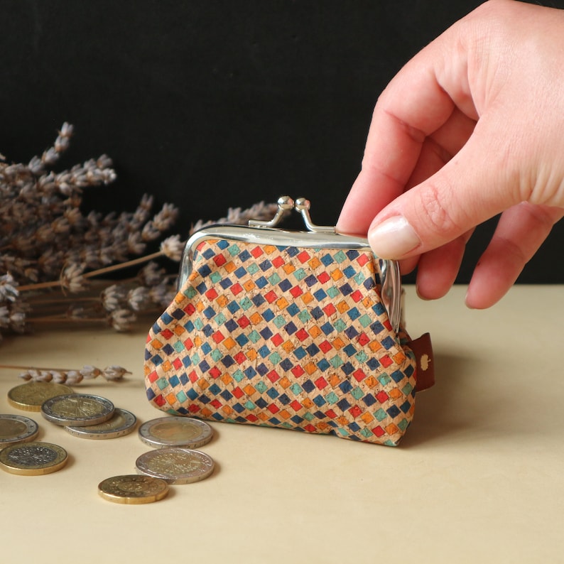 May include: A small, colorful coin purse with a geometric pattern. The purse is made of cork and has a silver metal frame with a snap closure.