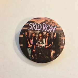 May include: Round button featuring the band Skid Row with a sunset background. The button displays a group of six people with long hair. The band's name is printed in white, stylized text.