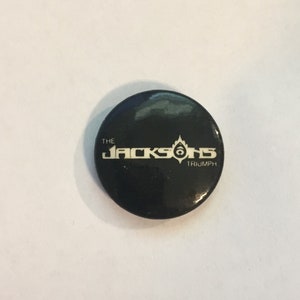 May include: A black button with a white logo that reads "The Jacksons Triumph".