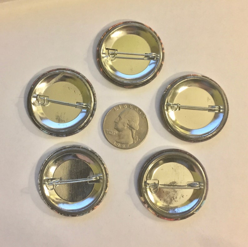 May include: Five round pinback buttons with safety pin backs are arranged around a quarter coin. The buttons have a colorful design around the edges. The quarter is dated 1982.