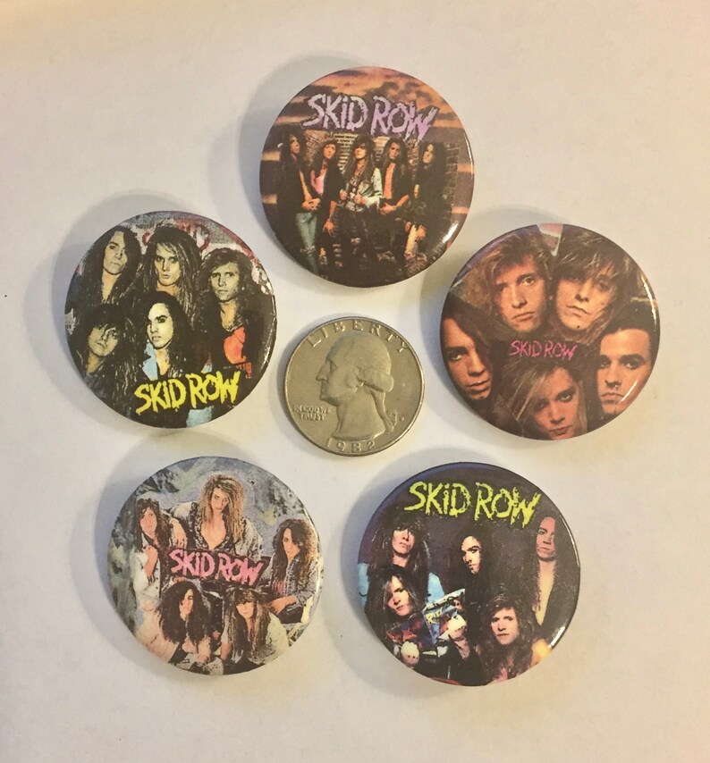 May include: A collection of five Skid Row band buttons. Each button features a different image of the band members, with the band's name prominently displayed. The buttons are round and have a glossy finish. A quarter is included for size comparison.