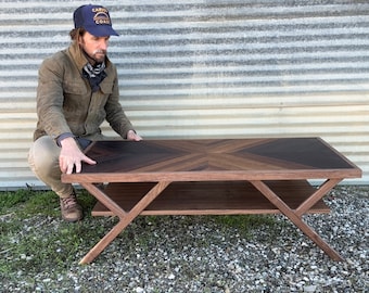 Puede incluir: Una mesa de centro de madera oscura con un patrón geométrico en la parte superior. La mesa tiene un estante inferior y patas inclinadas.