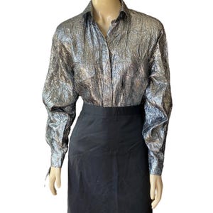 May include: A silver metallic long-sleeved button-up shirt with a textured pattern. The shirt is paired with a black skirt.