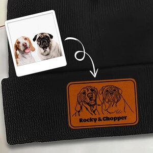May include: Black beanie with a brown leather patch featuring dog illustrations and the text "Rocky & Chopper." A small photo of two dogs is in the upper left corner. The beanie is made of a soft, knitted material.