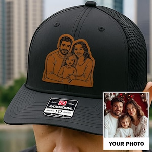 May include: Black trucker hat with a mesh back and a brown leather patch featuring a family portrait. The hat has a curved brim and an adjustable strap. The Richardson brand label is visible on the front.