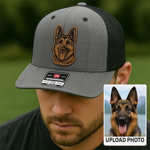May include: A gray and black trucker hat with a leather patch featuring a German Shepherd dog. The hat has a curved brim and a mesh back. The patch is brown and tan, and the hat has a Richardson 112 tag.