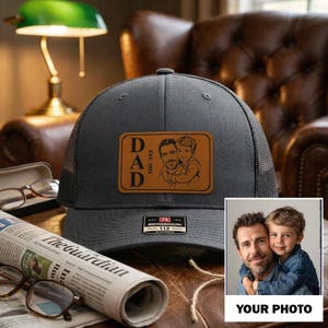 May include: A gray trucker hat with a mesh back and a leather patch. The patch features the word "DAD" and a sketch of a father and child. The hat has a Richardson 112 tag. A photo of a father and child is shown below the hat.